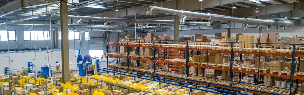 Großes Lager mit hohen Regalen, gestapelten Kartons und gelben Kisten, organisiert für effiziente Logistik.
