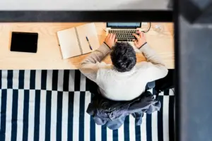 Person arbeitet an einem Laptop an einem Schreibtisch mit Notizbuch und Tablet.