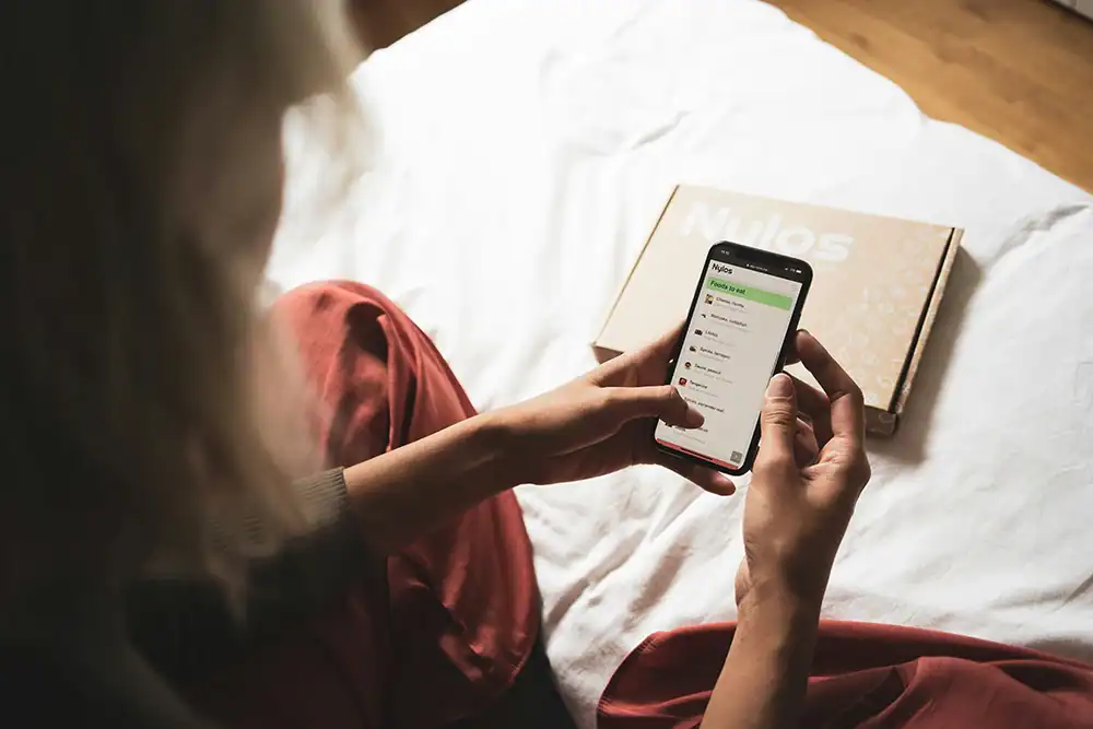Person nutzt Smartphone-App zur Auswahl personalisierter Produkte neben Versandpaket.
