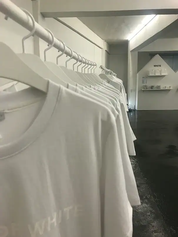 Weiße T-Shirts auf Kleiderbügeln in einer minimalistischen Produktions- oder Verkaufsfläche.