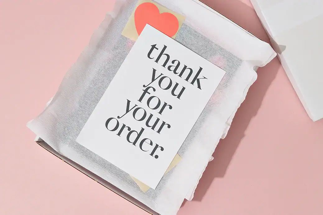 Verpacktes Produkt mit Karte thank you for your order auf rosa Hintergrund.