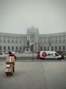 DPD-Zusteller mit Paketen vor historischem Gebäude in urbaner Umgebung.