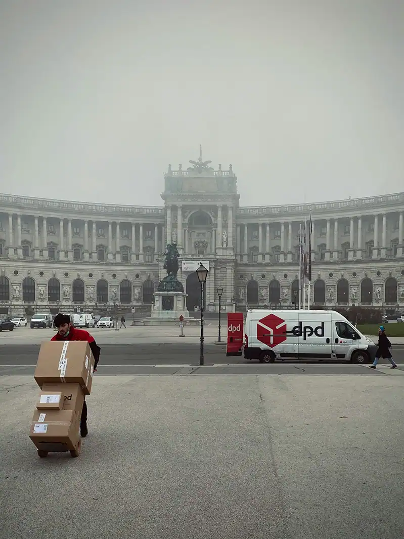 DPD-Zusteller mit Paketen vor historischem Gebäude in urbaner Umgebung.