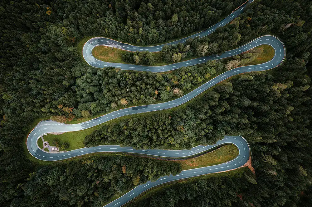 Luftaufnahme einer kurvenreichen Straße durch dichten Wald.