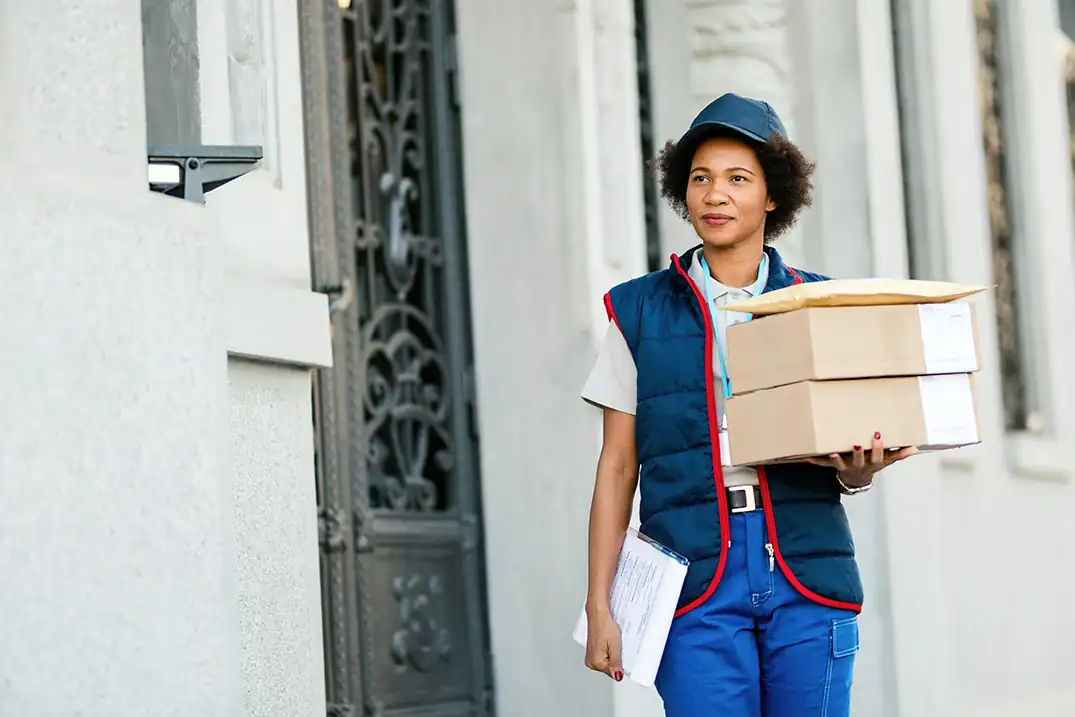 Paketzustellerin mit mehreren Sendungen vor einem Hauseingang.