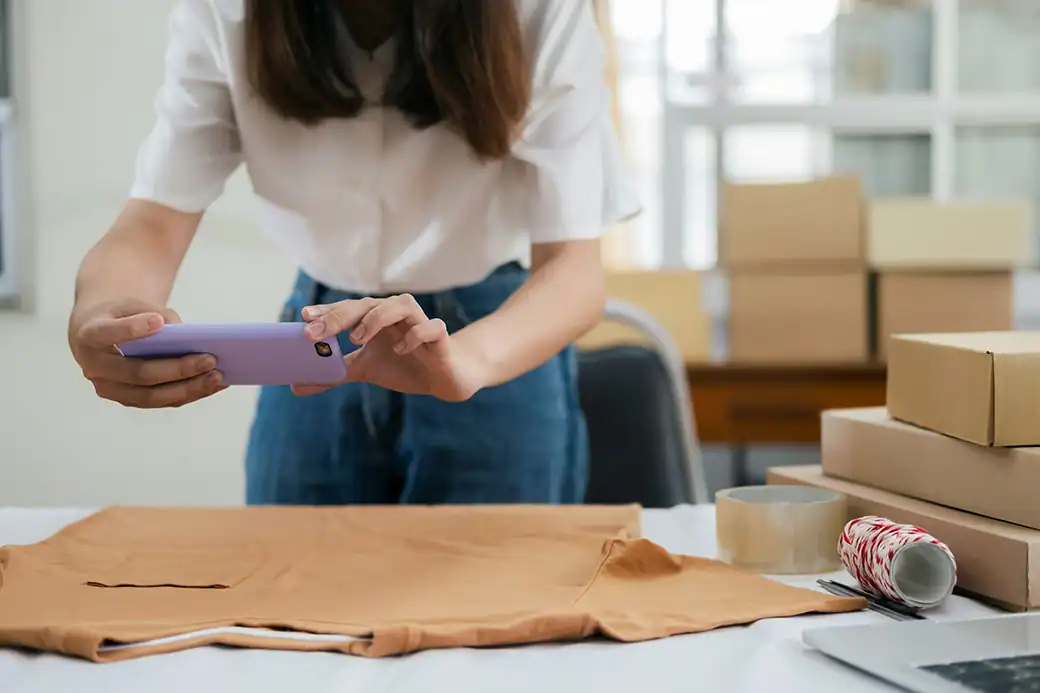 Frau fotografiert ein T-Shirt mit dem Smartphone für ihren Onlineshop.